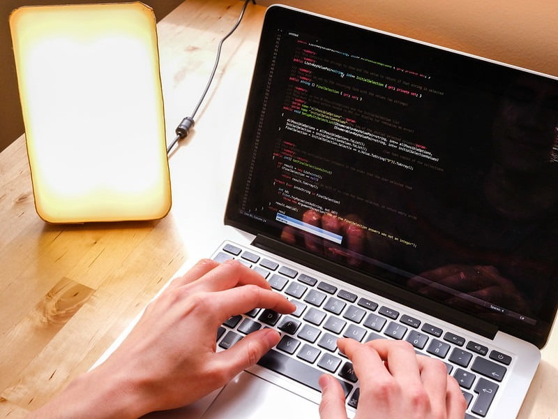 Person working on laptop with bright light therapy lamp next to them