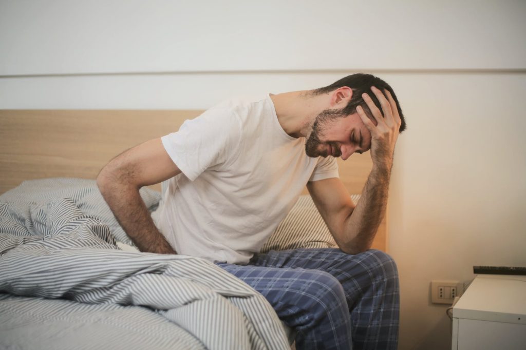 young man in sleepwear suffering from headache in morning due to sleep inertia