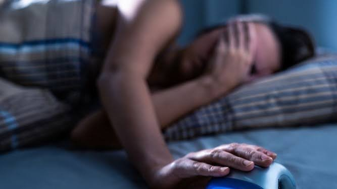 woman sleeping trying to turn off the alarm clock