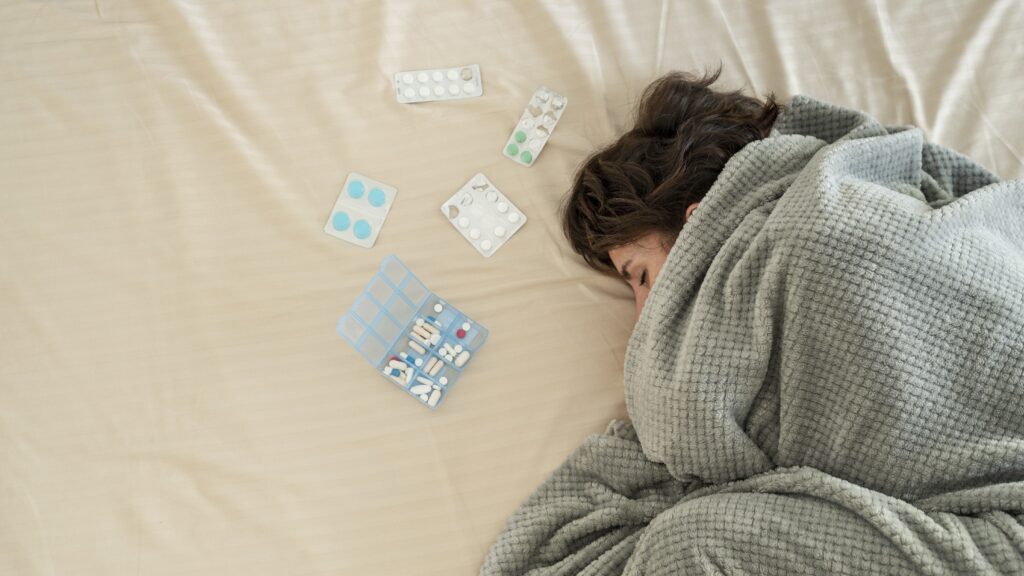 an insomniac woman sleeping with sleep medicines on her bed with blanket