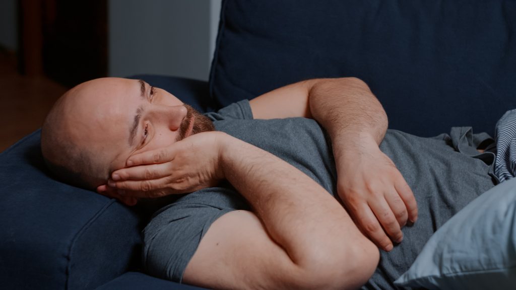 man lying awake and distressed on a couch representing the struggle of sleep anxiety