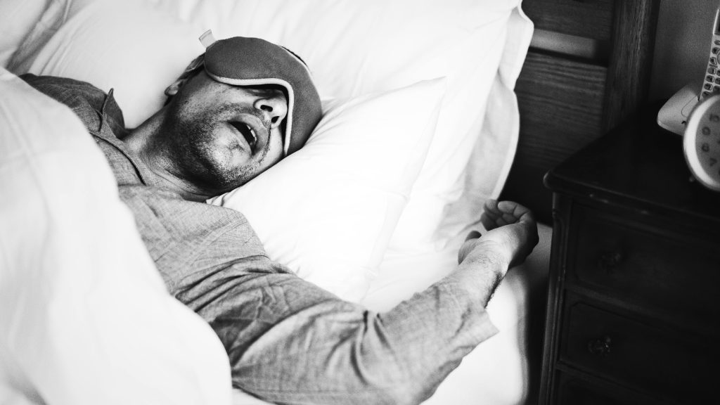 man wearing a sleep mask depicting a moment before or after a sudden body jerk while sleeping