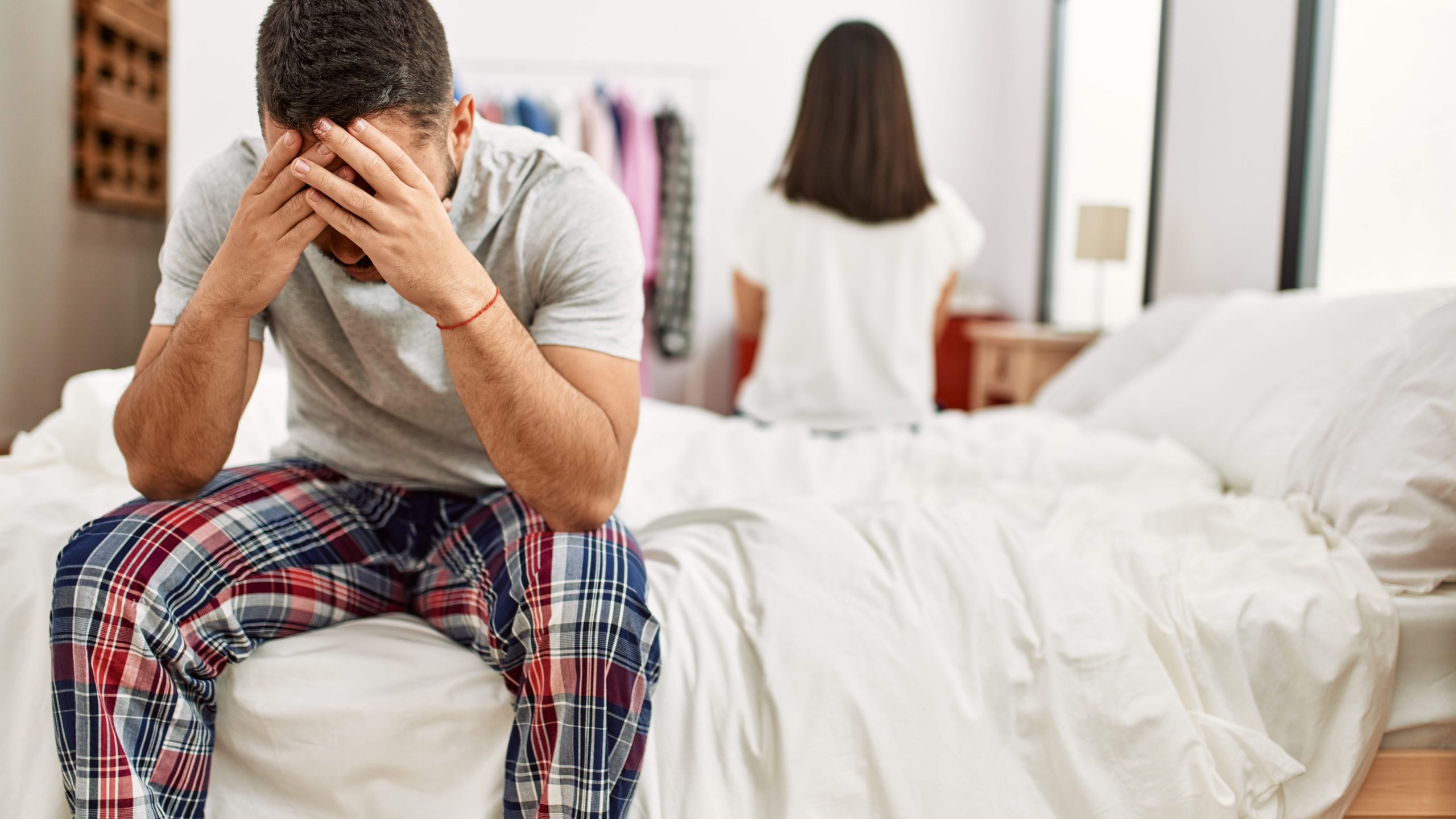 young couple sitting apart on a bed experiencing a bedtime conflict