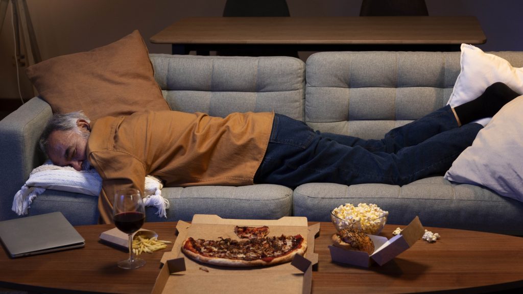 man sleeping on couch after eating pizza and drinking red wine placed on the table