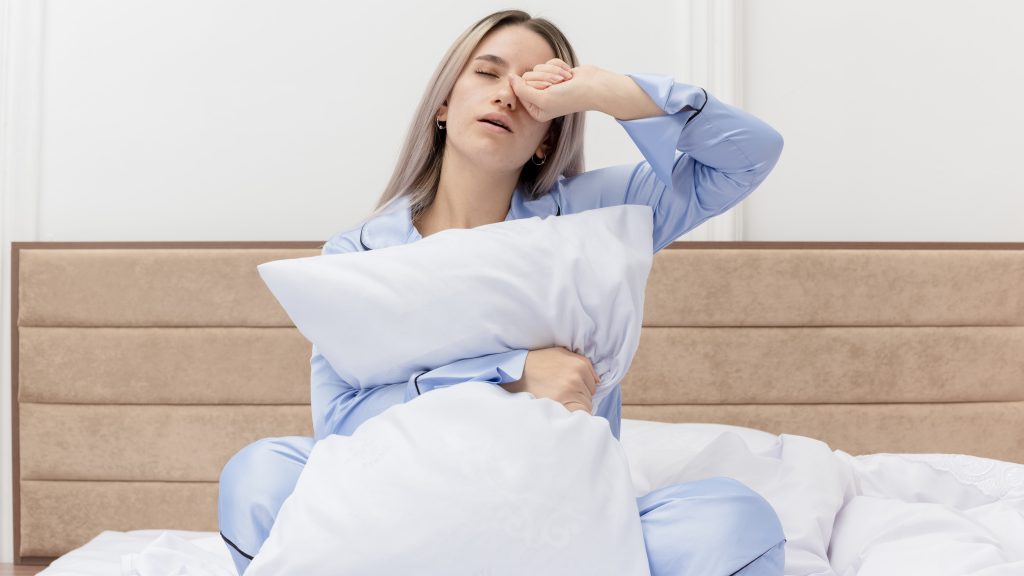 tired woman in sitting in bed and rubbing her eyes showing signs of needing rest 
