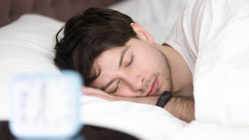 man sleeping while wearing a fitness tracker which can cause sleep tracker anxiety and orthosomnia