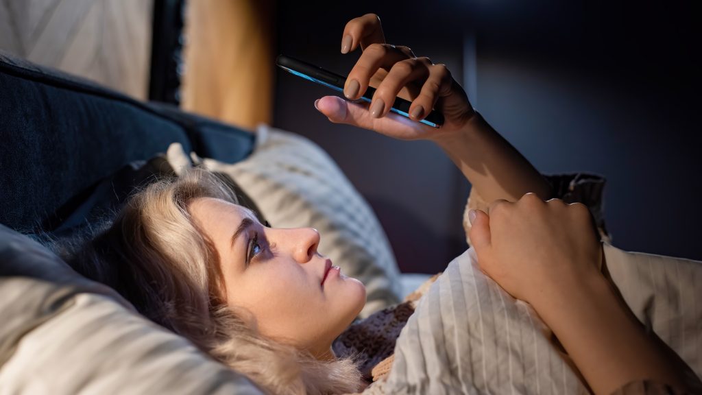 woman lying in bed using a smartphone which can lead to sleep score anxiety and sleep issues