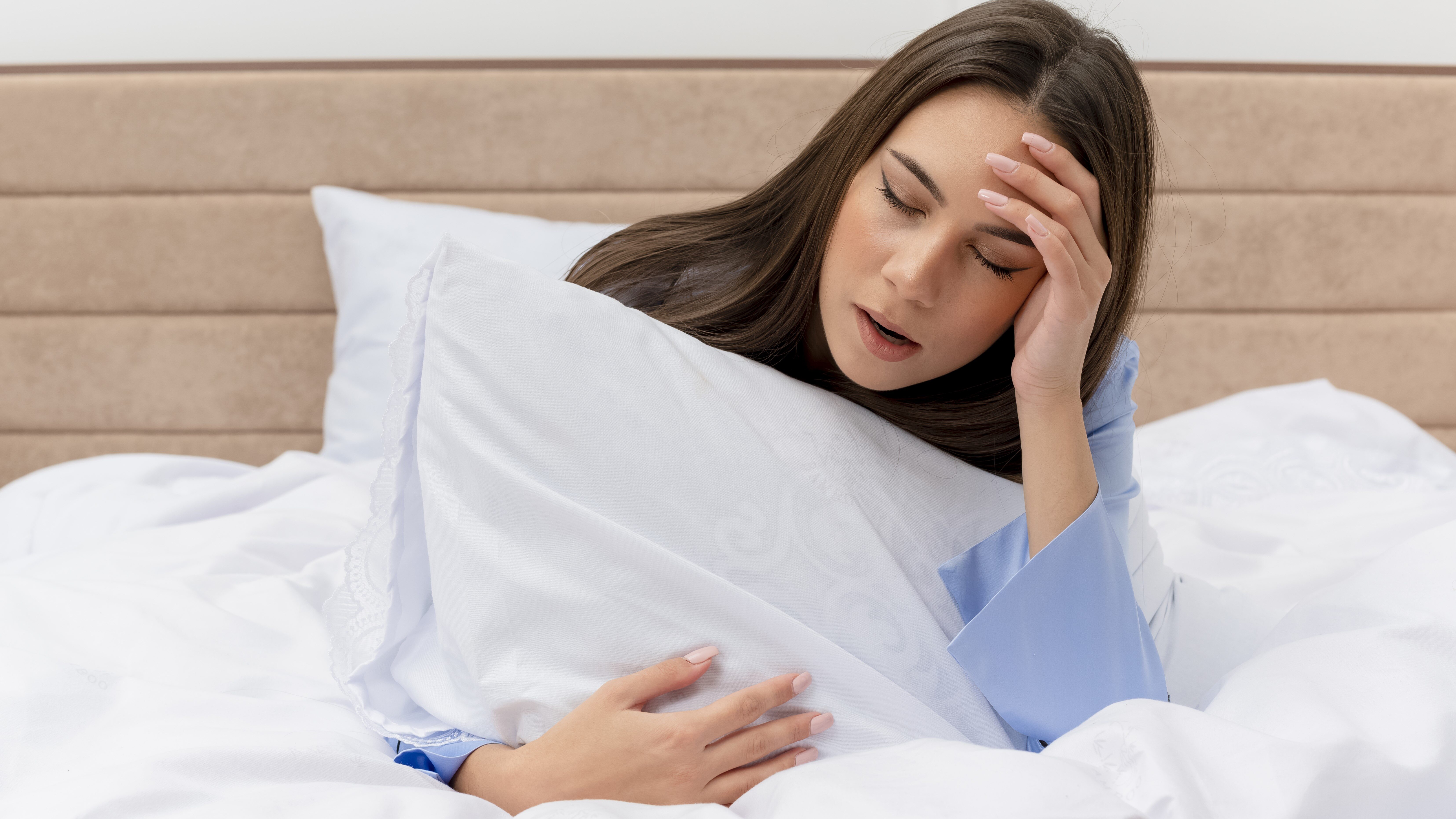 exhausted woman clutching a pillow in bed while struggling with chronic insomnia