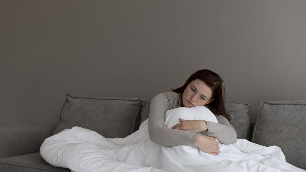 pregnant woman sitting on sofa wrapped in blanket struggling with insomnia