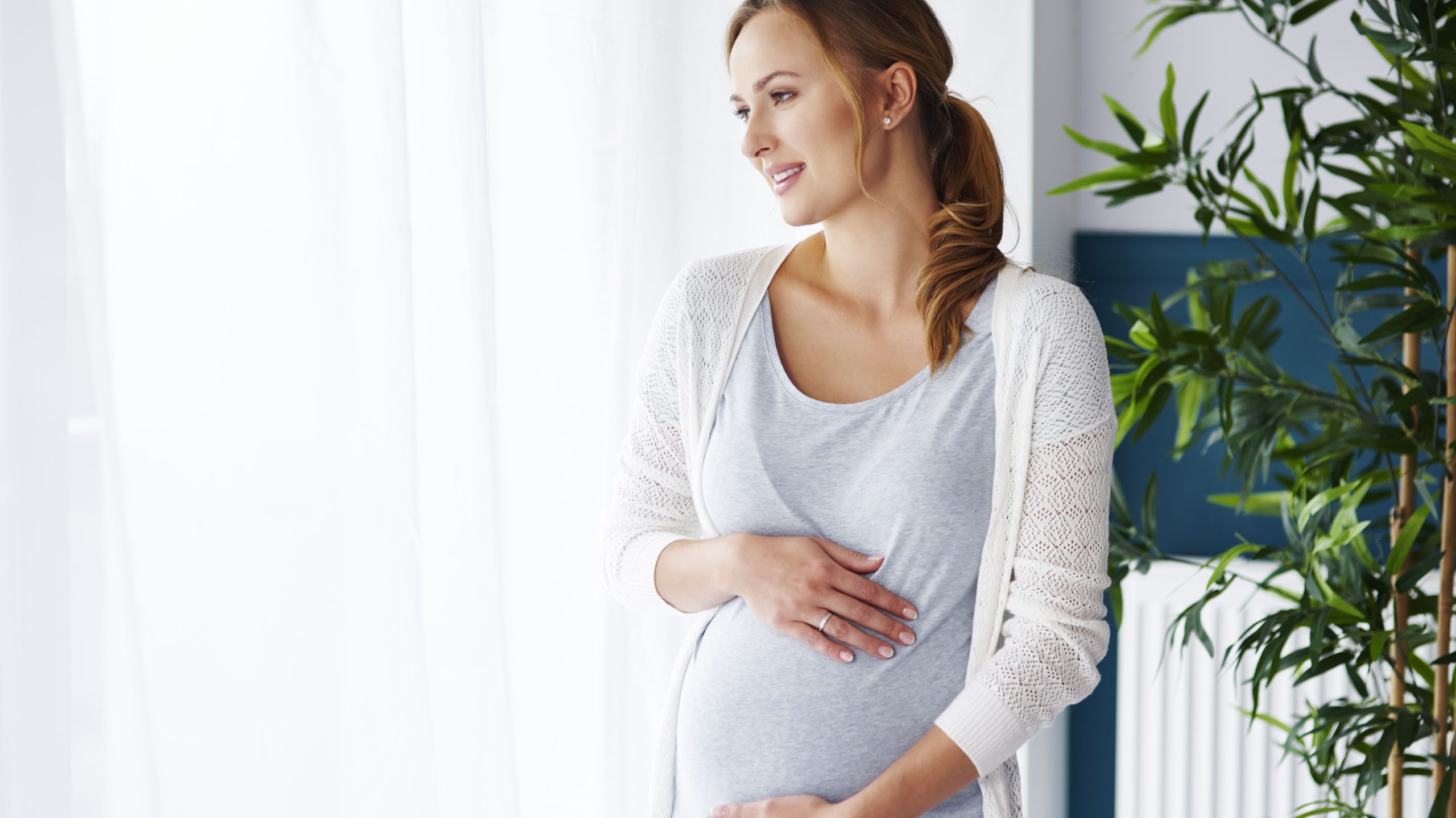 pregnant woman holding her belly near a bright window