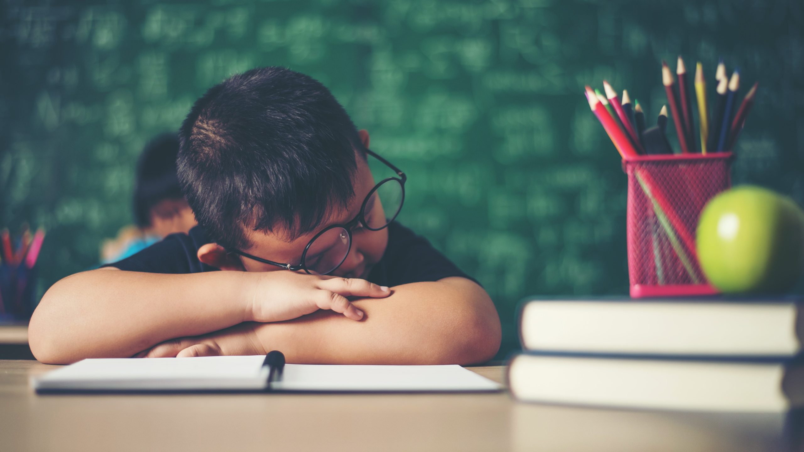 tired young boy asleep on his classroom desk showing the impact of sleep deprivation and sudden schedule changes