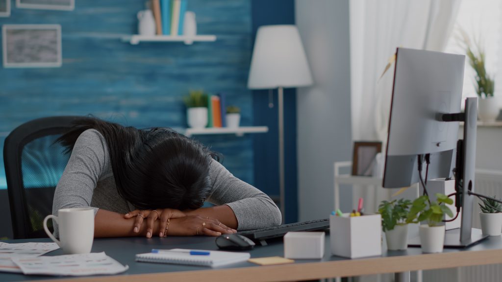 overworked woman resting her head next to a computer screen due to chronic sleep issues