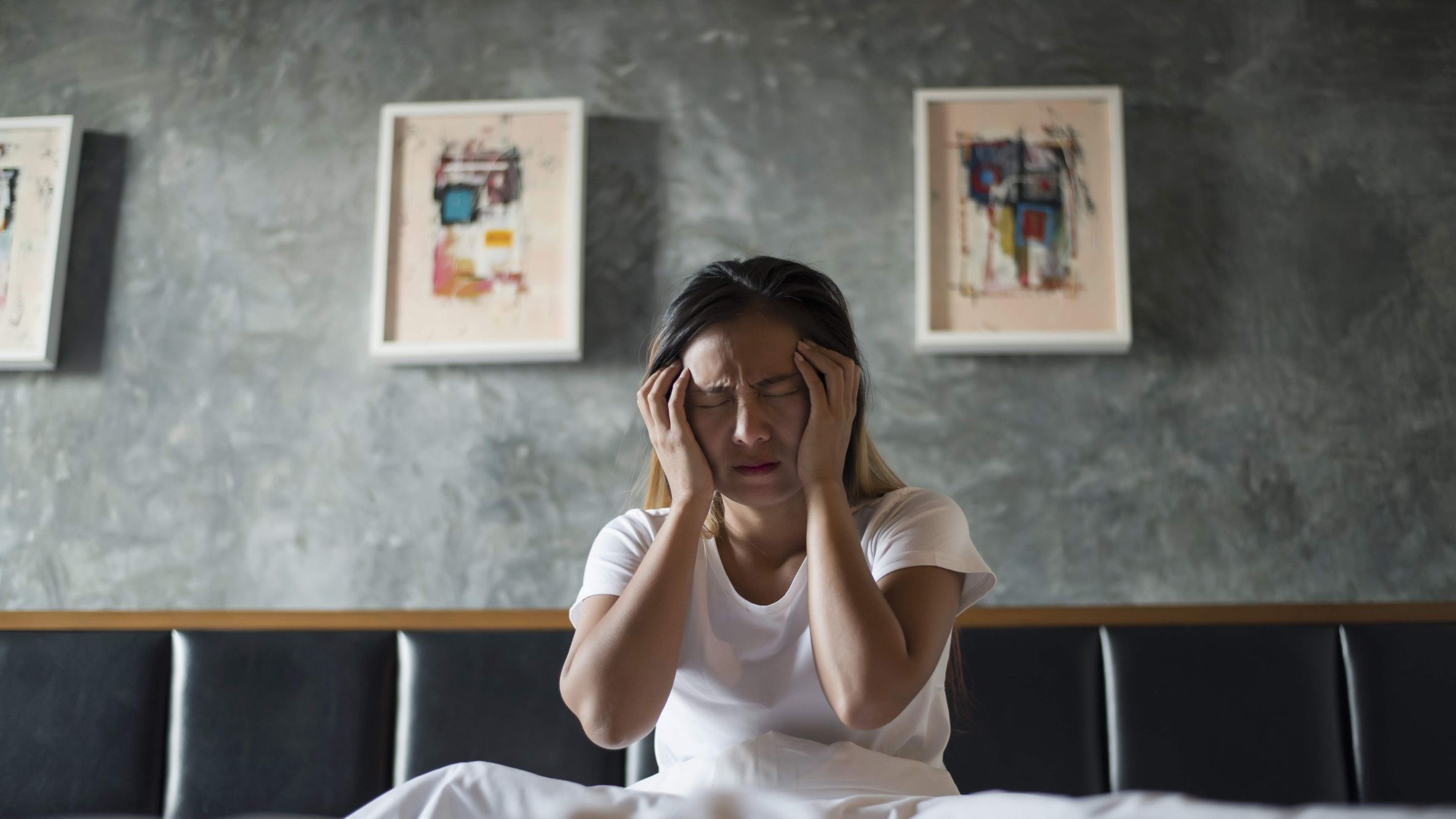 frustrated woman sitting in bed holding her head due to poor sleep and fatigue