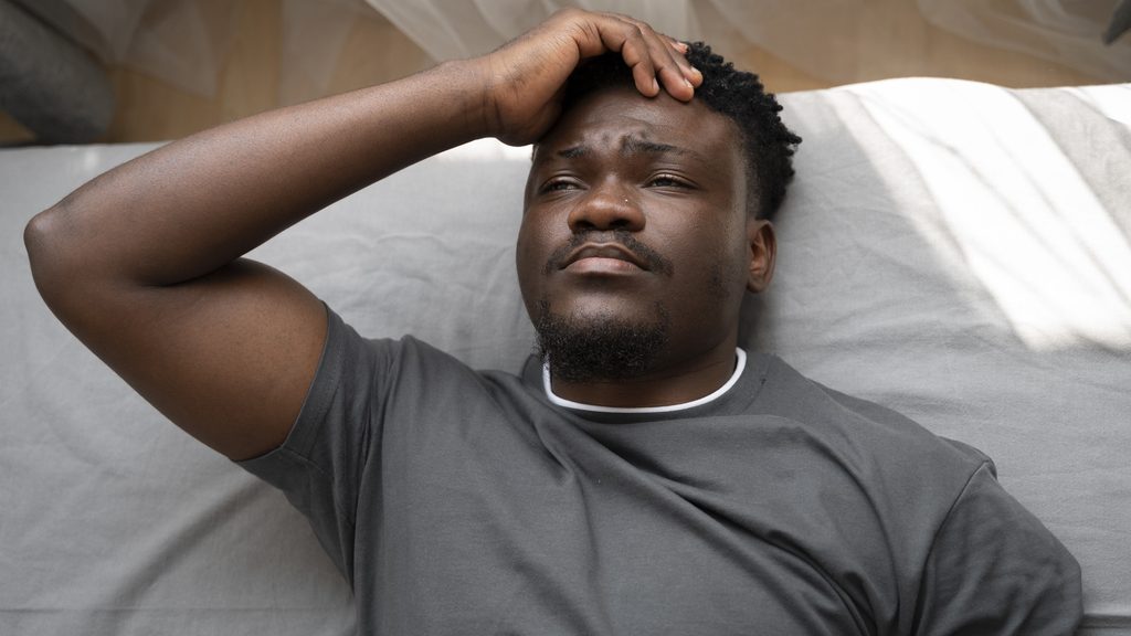 man lying awake in bed experiencing sleep disruptions and restless thoughts