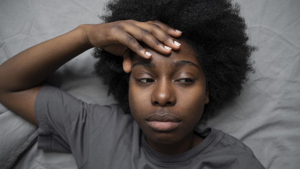 awake person in bed holding forehead due to late night sleep anxiety and overactive mind
