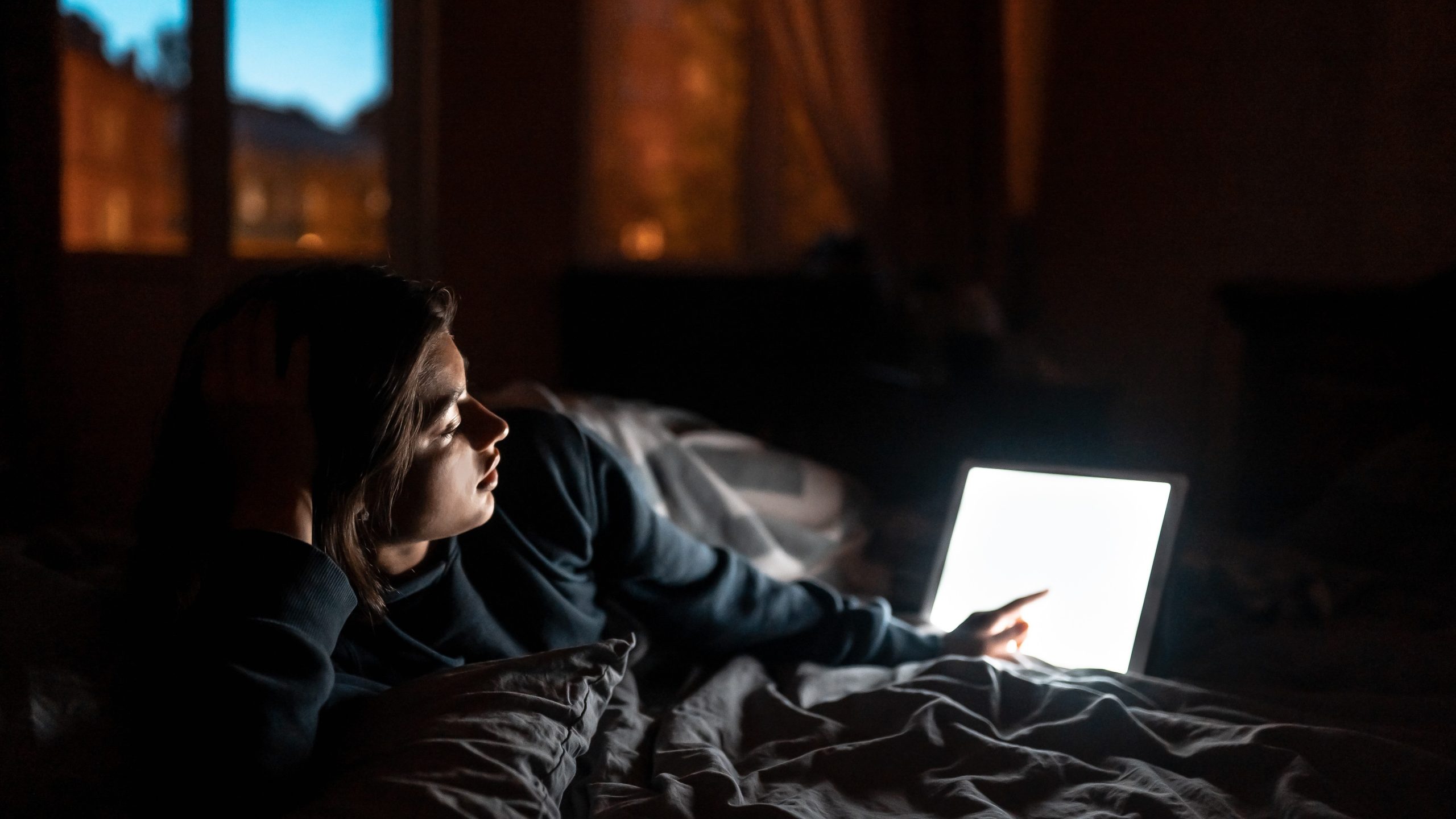 woman lying awake using bright screen illustrating sleep disruption in winter darkness